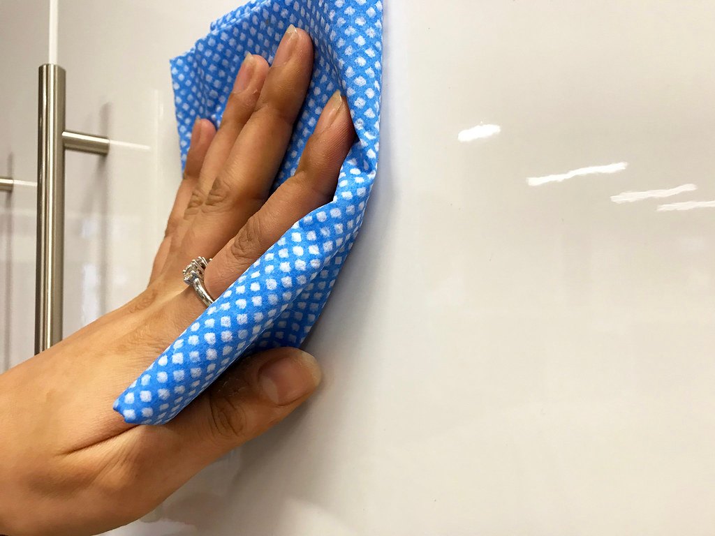 Hands using a cloth to wipe a white kitchen cabinet beside a counter.