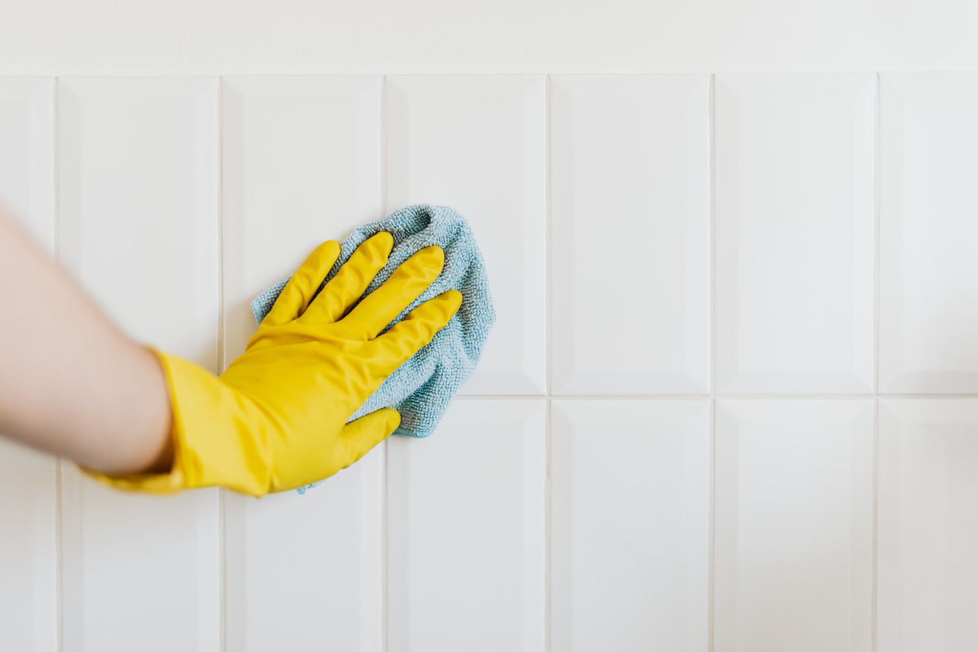 A yellow-gloved hand wiping an installed tiled wall with a cloth.