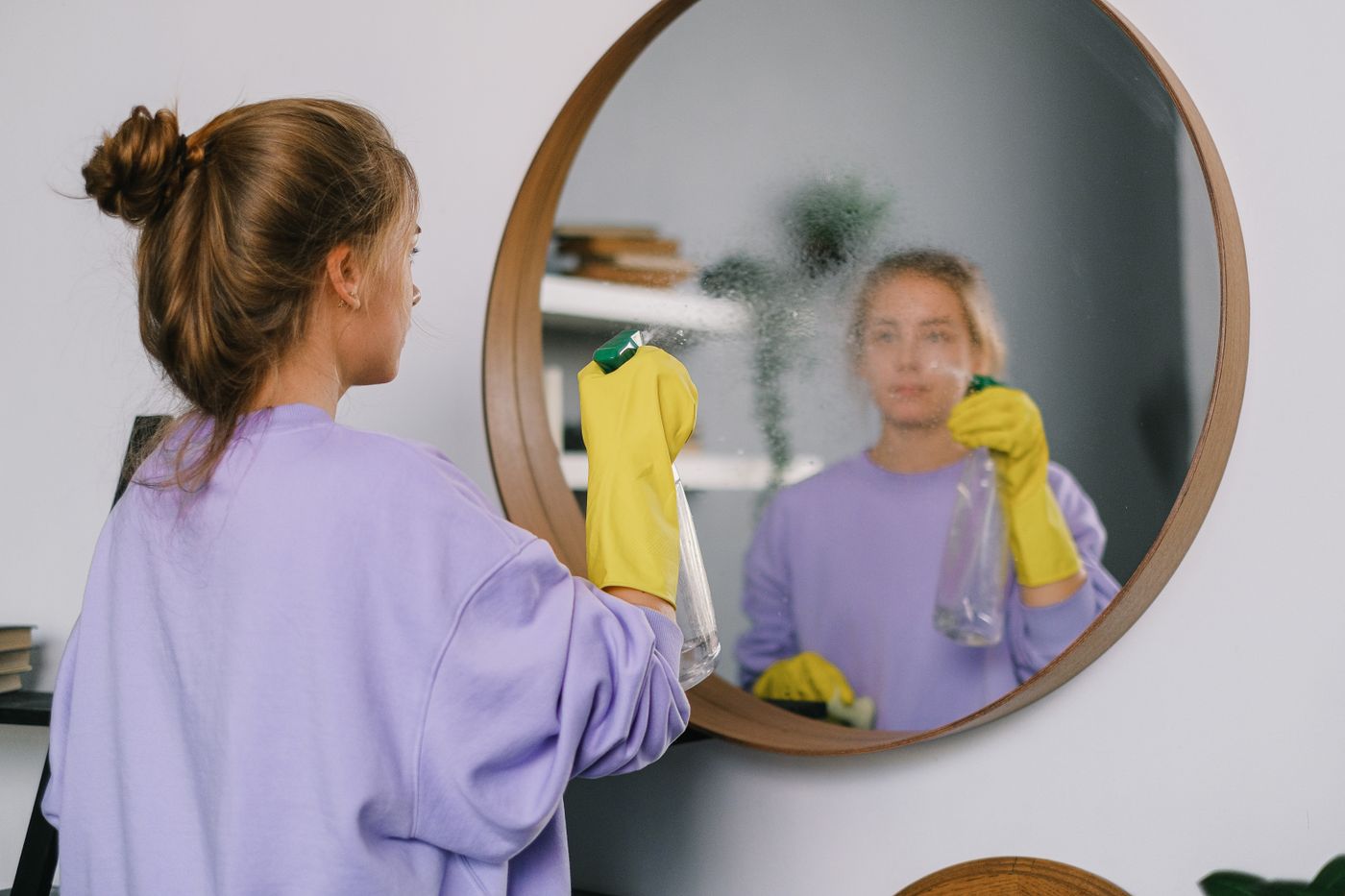 A woman holding a clear spray bottle near an interior mirror.