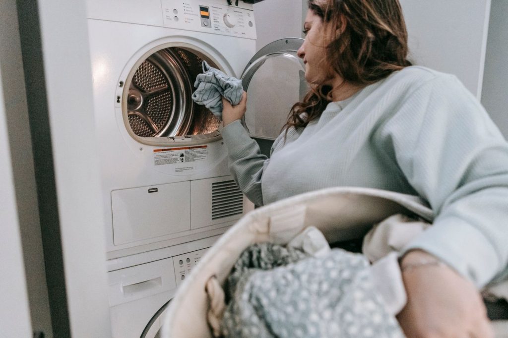 A person handling household laundry beside stacked laundry appliances.