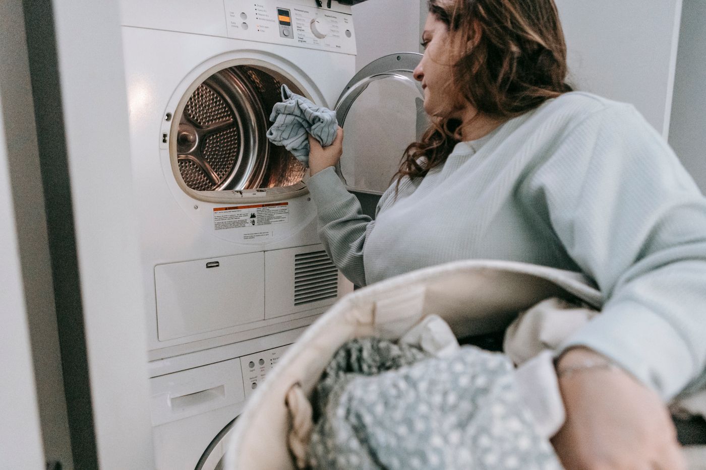 A person handling household laundry beside stacked laundry appliances.