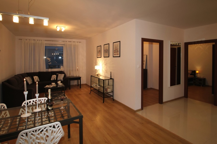 A furnished living and dining room with a dark sofa, table, chairs, and hard flooring
