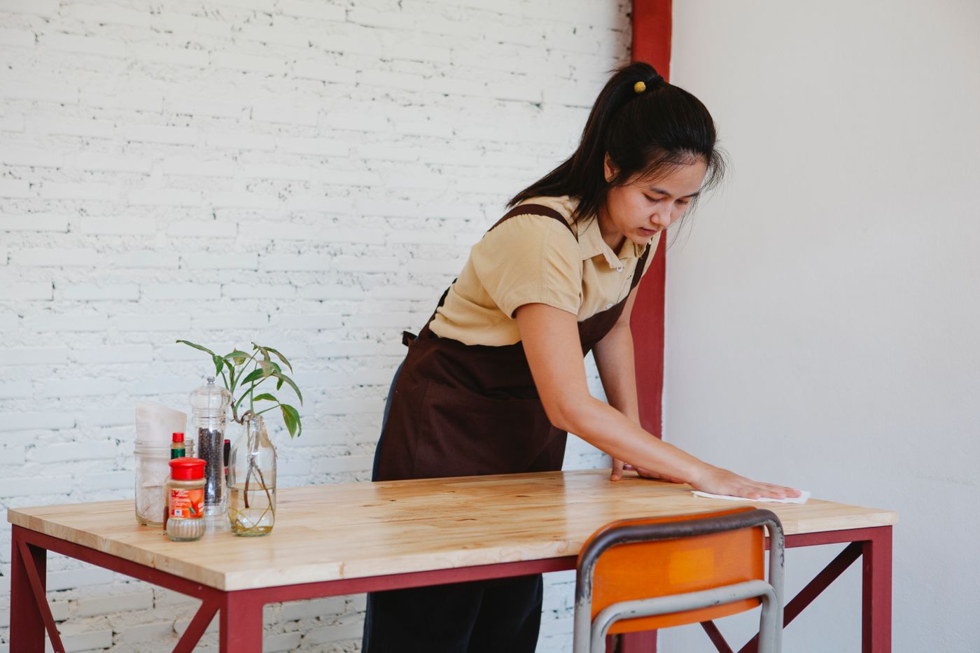A woman wiping a wooden table in a furnished shared interior.
