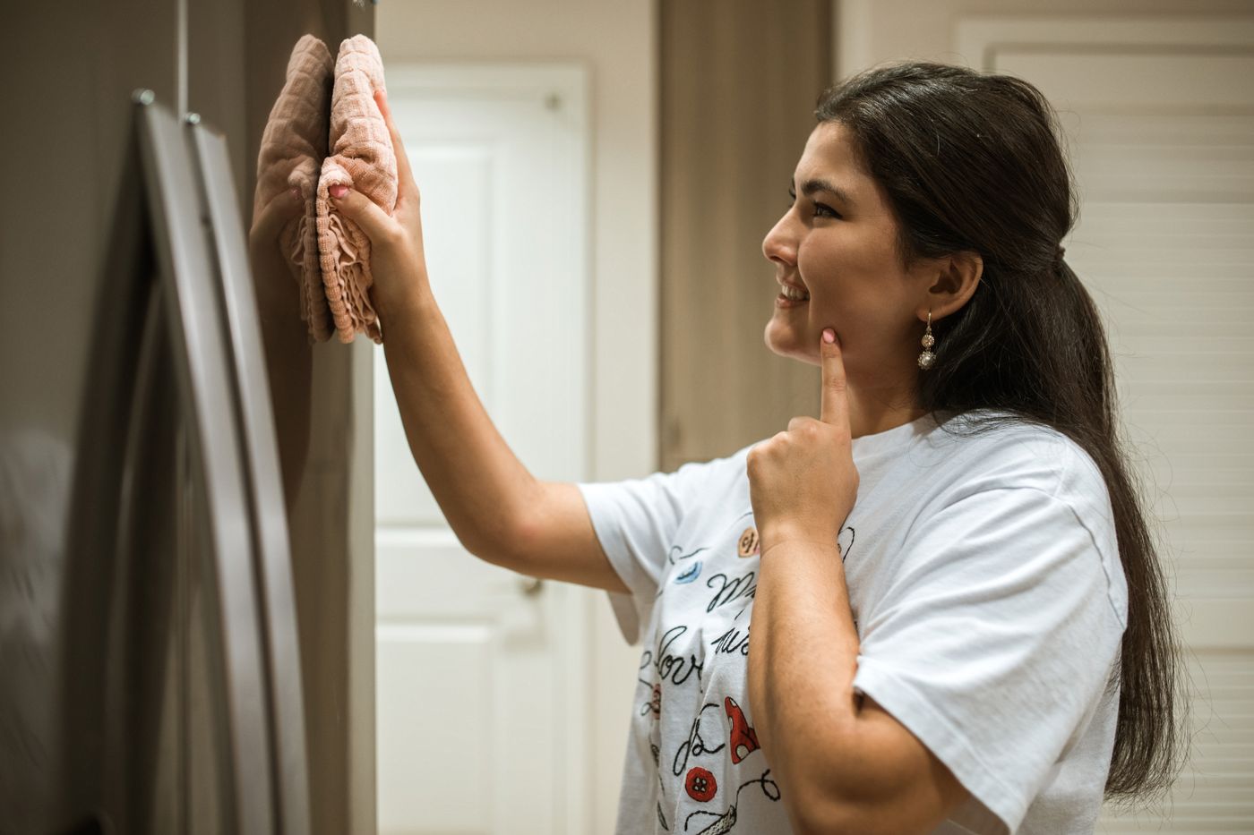 A woman wiping a metal-looking refrigerator door with a cloth in a kitchen.