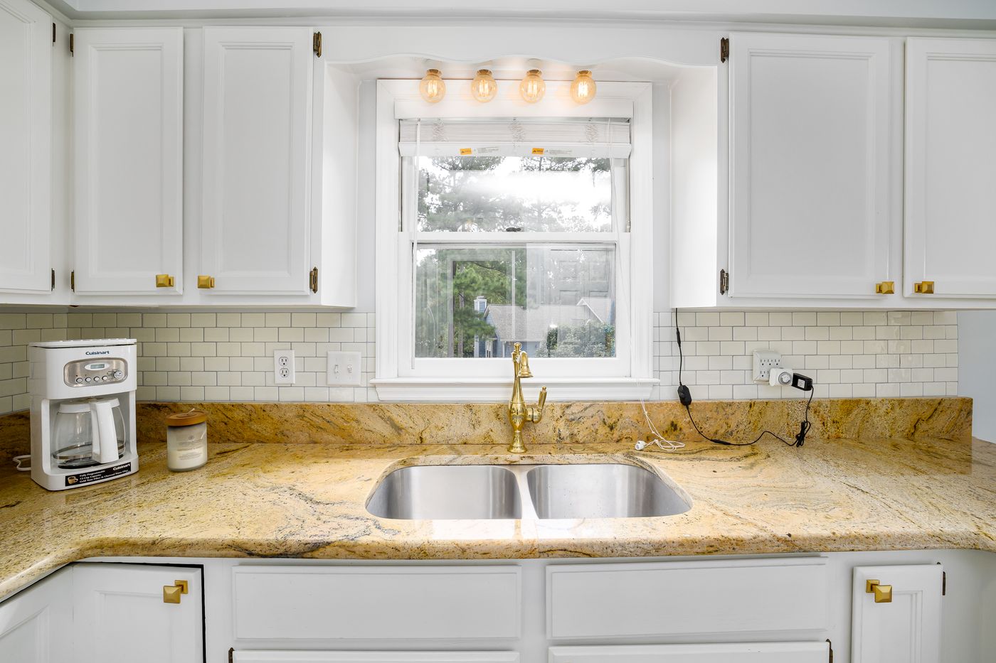 A furnished kitchen with a patterned countertop, sink, coffee maker and wall fixtures.