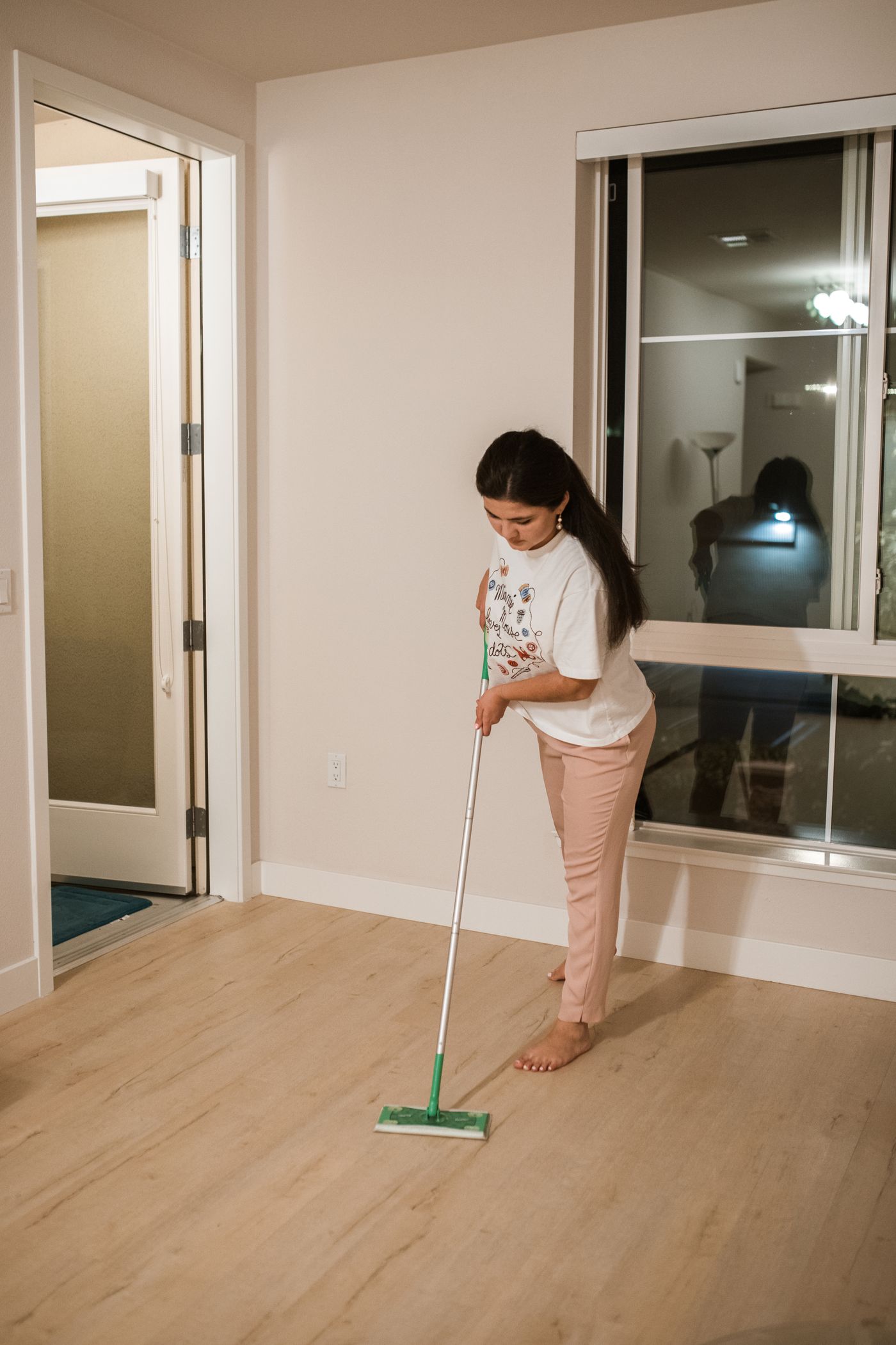 A woman moving a flat cleaning tool across a wood-pattern floor in a room.